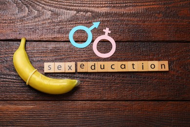 Photo of Phrase Sex Education made of wooden letters, banana with condom, paper female and male gender symbols on table, flat lay