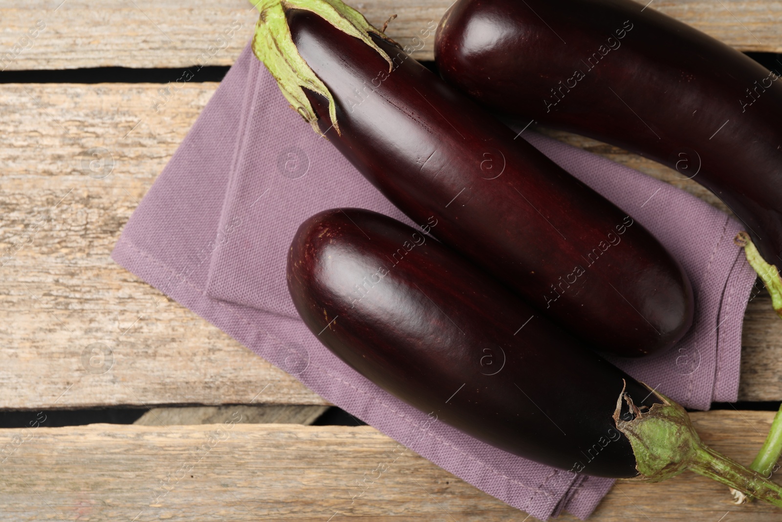 Photo of Many ripe eggplants and towel on wooden table, flat lay