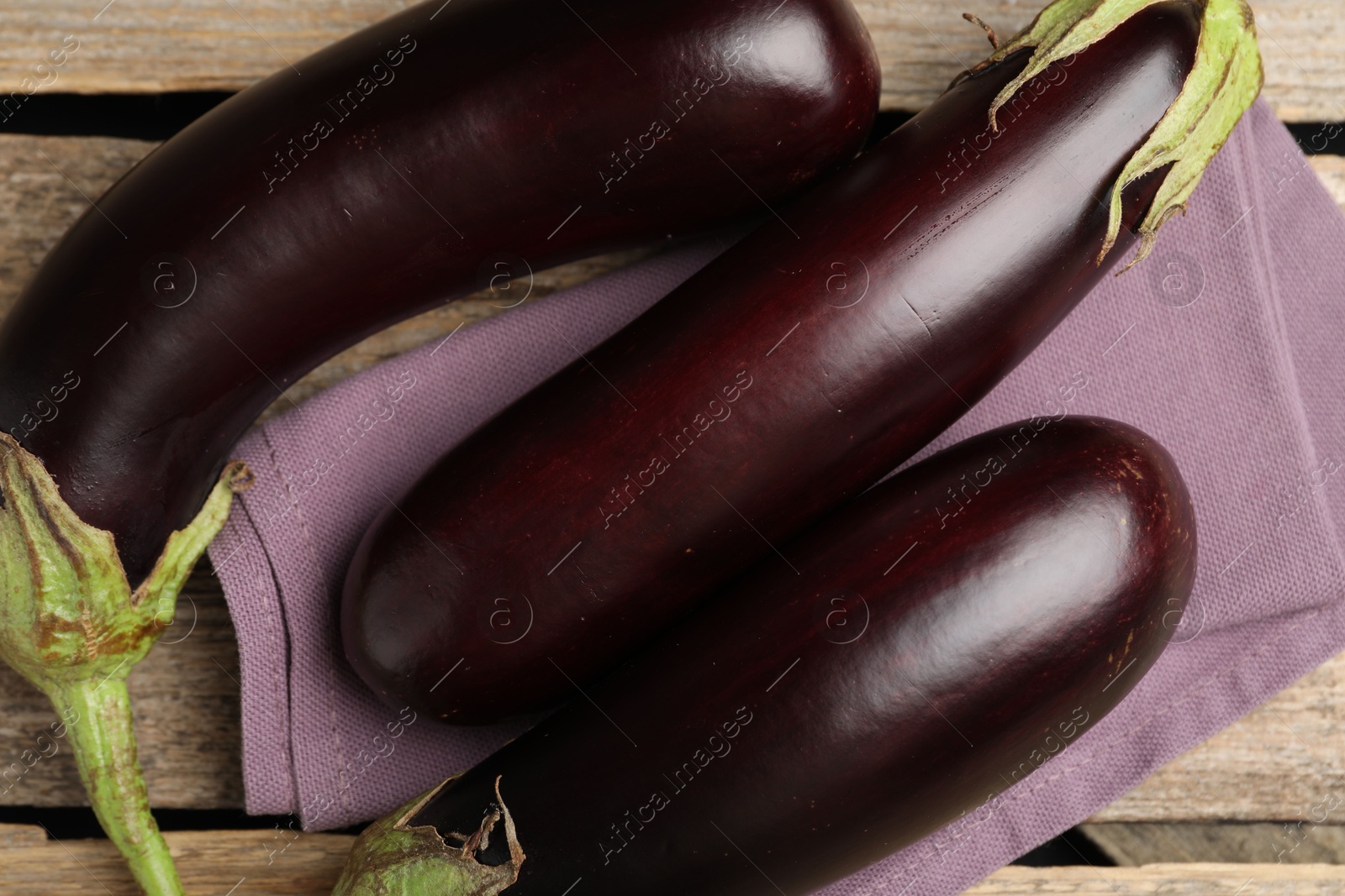 Photo of Many ripe eggplants and towel on wooden table, flat lay
