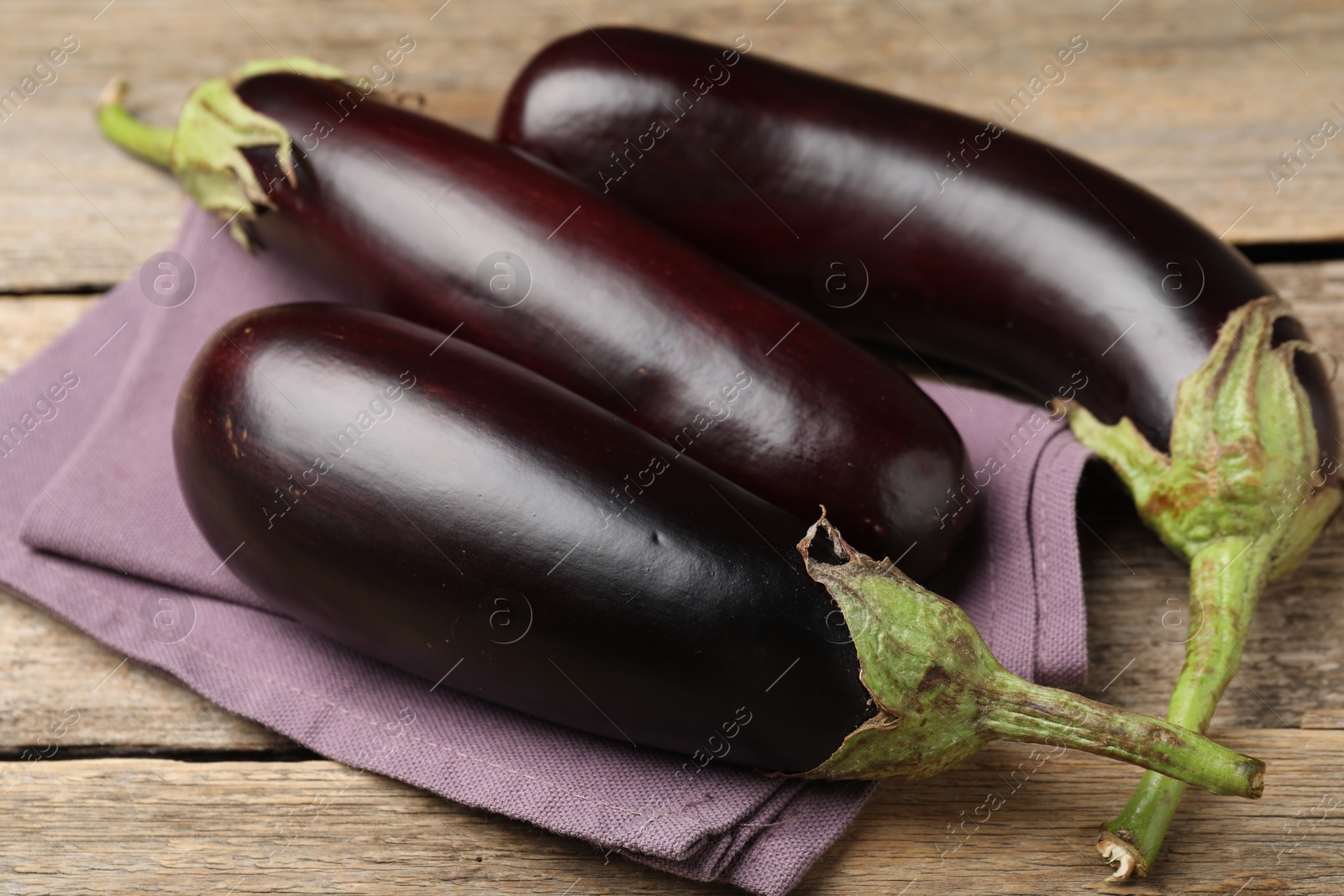 Photo of Many ripe eggplants and towel on wooden table, closeup