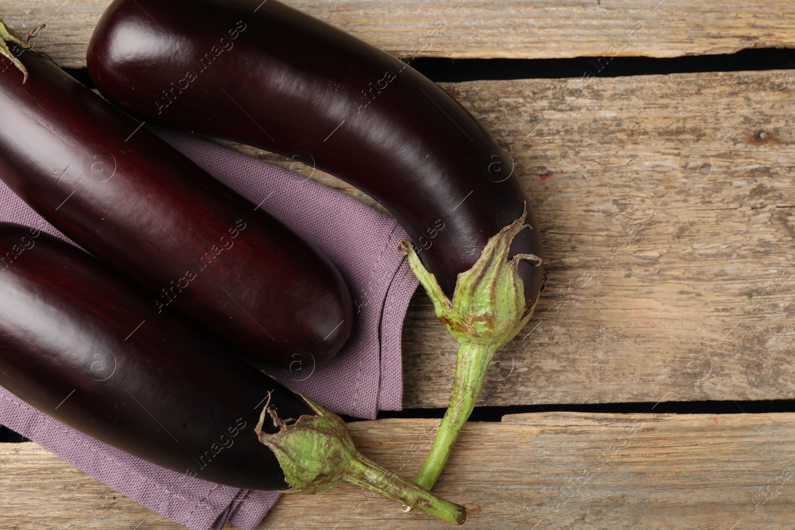 Photo of Many ripe eggplants and towel on wooden table, flat lay. Space for text