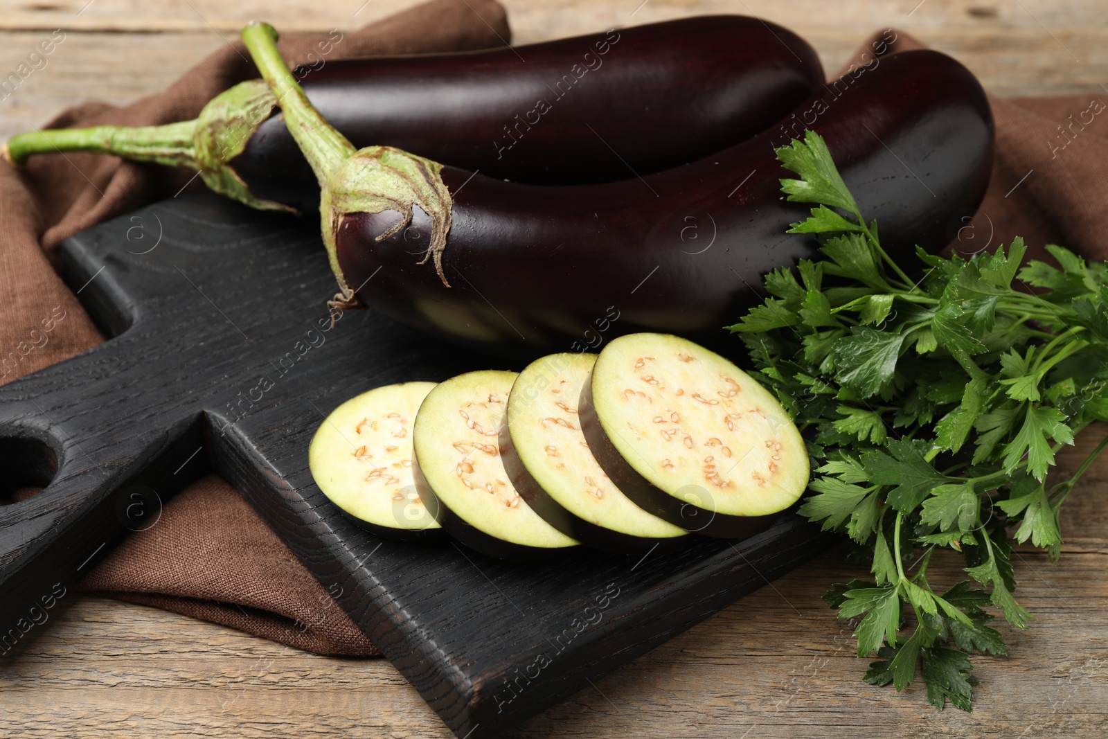 Photo of Whole and cut eggplants with parsley on wooden table, closeup