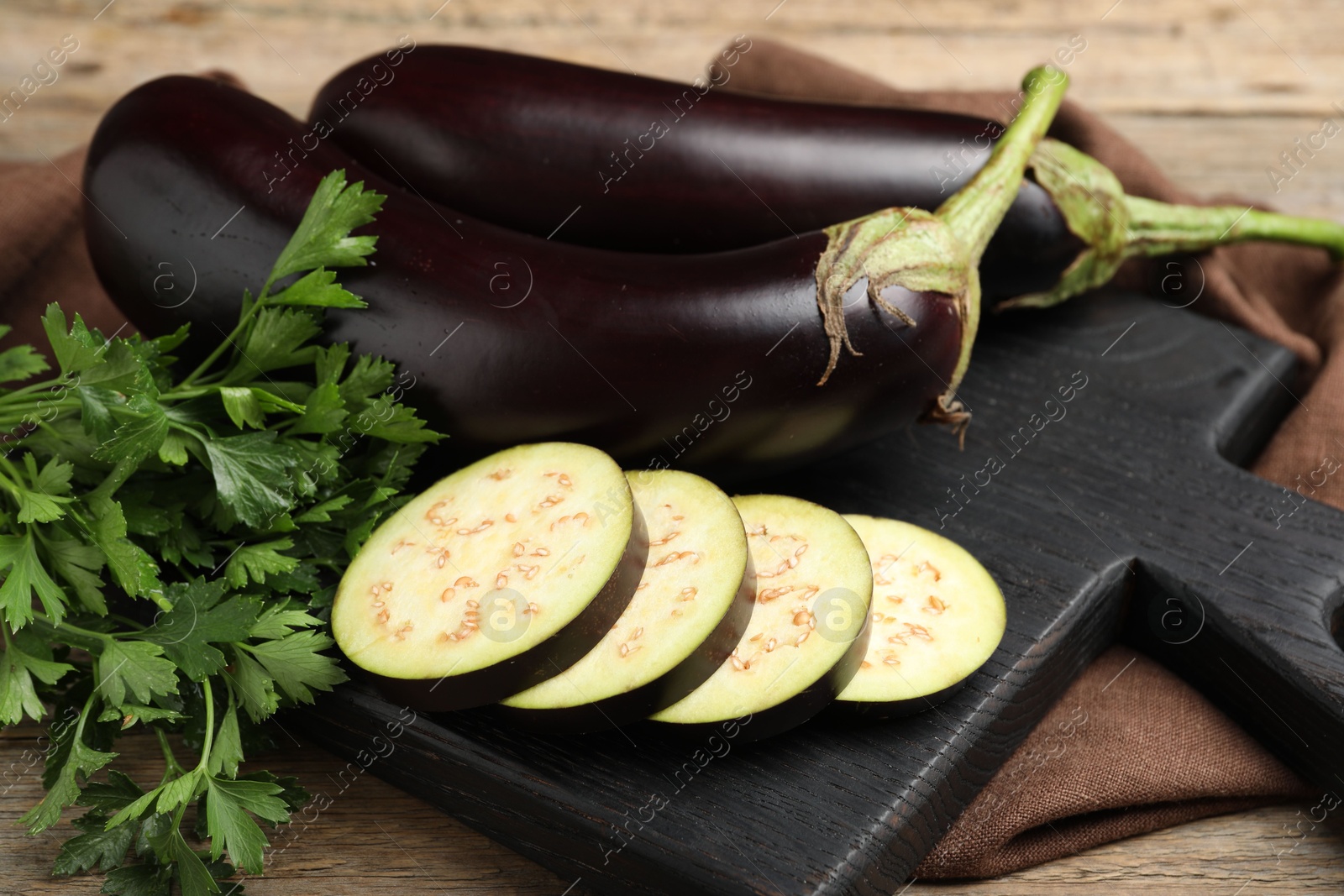 Photo of Whole and cut eggplants with parsley on wooden table, closeup