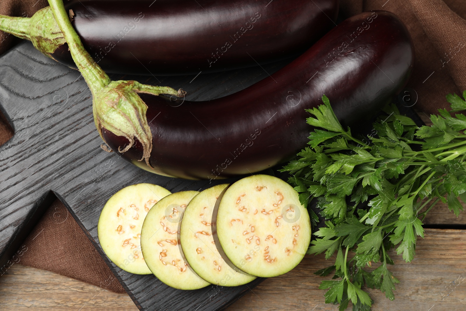 Photo of Whole and cut eggplants with parsley on wooden table, flat lay