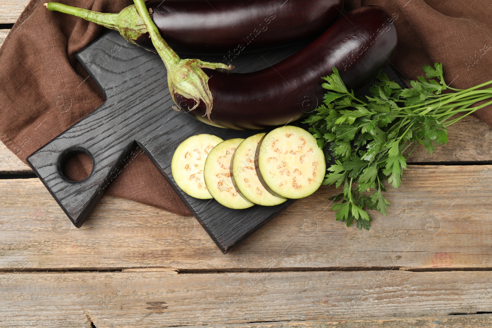 Photo of Whole and cut eggplants with parsley on wooden table, flat lay. Space for text