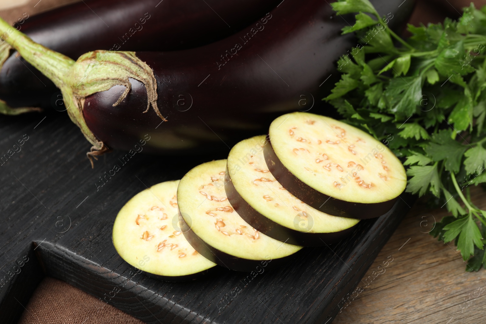 Photo of Whole and cut eggplants with parsley on wooden table, closeup