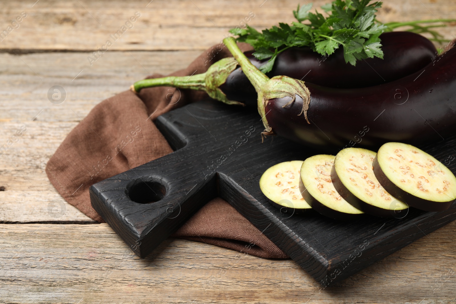 Photo of Whole and cut eggplants with parsley on wooden table, closeup