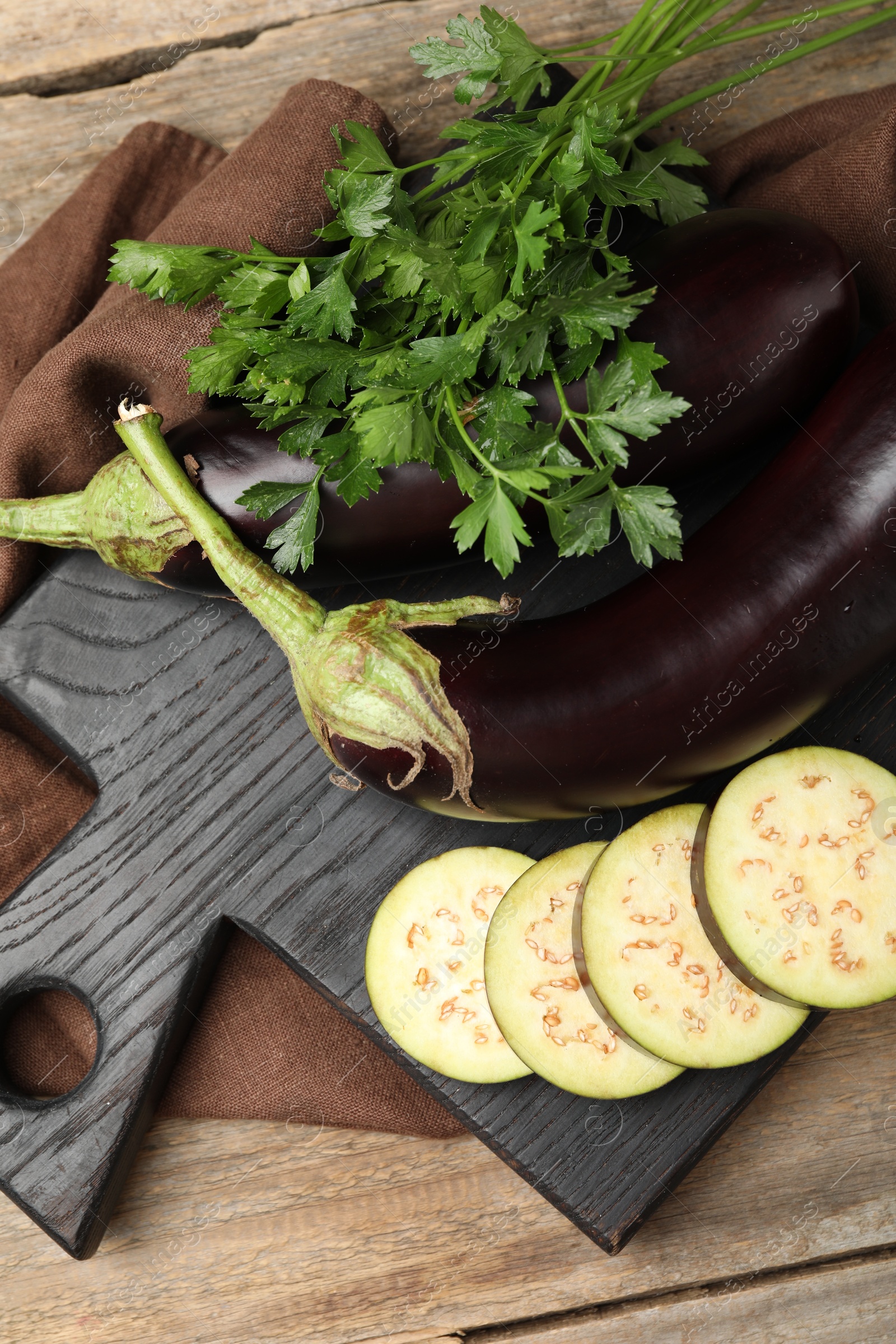 Photo of Whole and cut eggplants with parsley on wooden table, flat lay