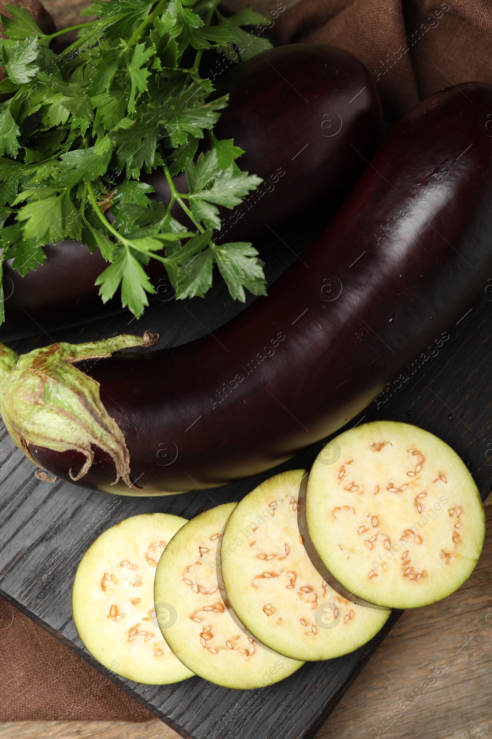 Photo of Whole and cut eggplants with parsley on wooden table, flat lay