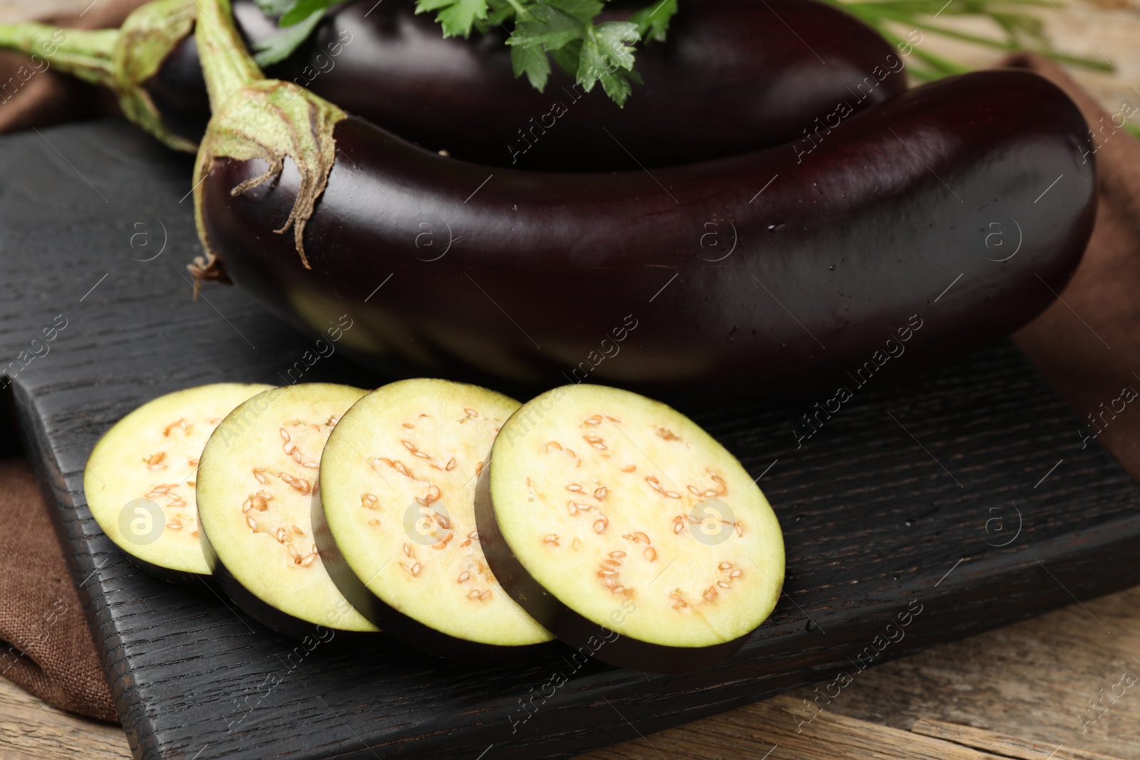 Photo of Whole and cut eggplants with parsley on wooden table, closeup