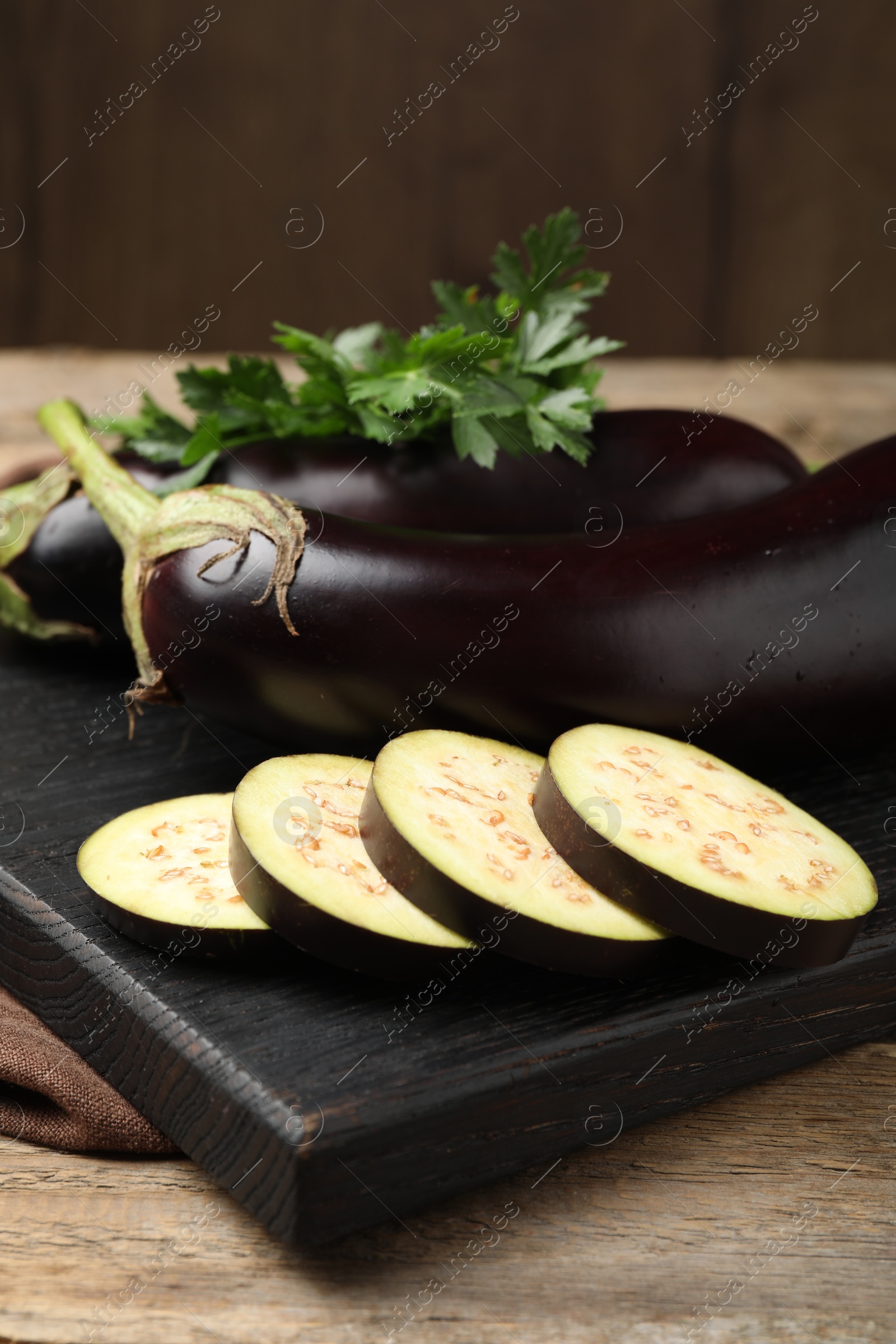 Photo of Whole and cut eggplants with parsley on wooden table, closeup