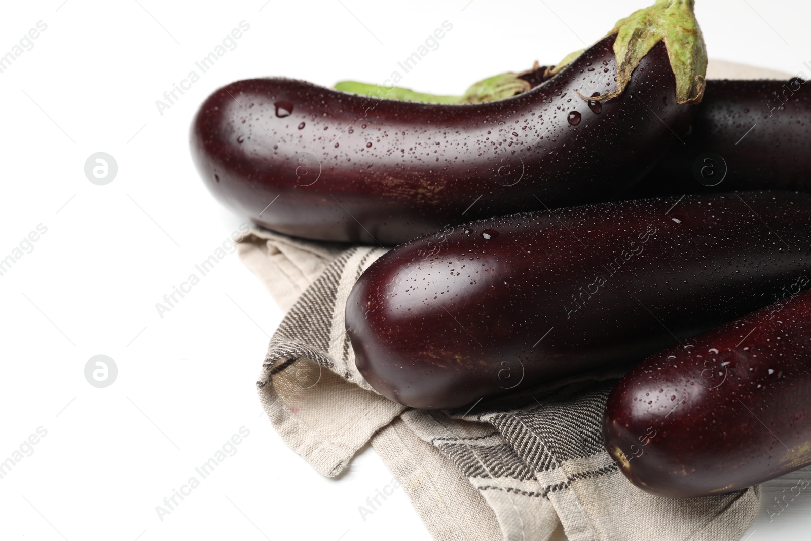 Photo of Many wet ripe eggplants and towel on white table, closeup