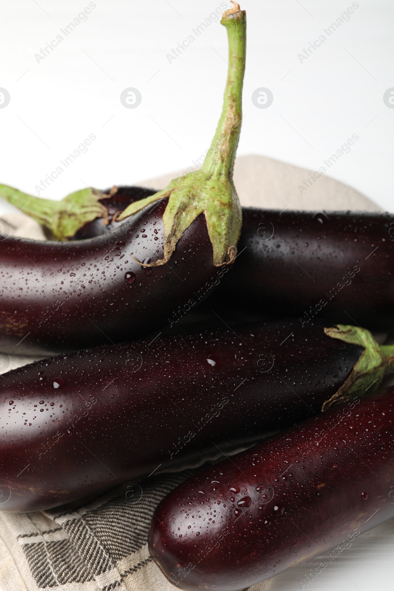 Photo of Many wet ripe eggplants and towel on white table, flat lay