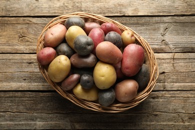 Photo of Different types of potatoes in wicker basket on wooden table, top view