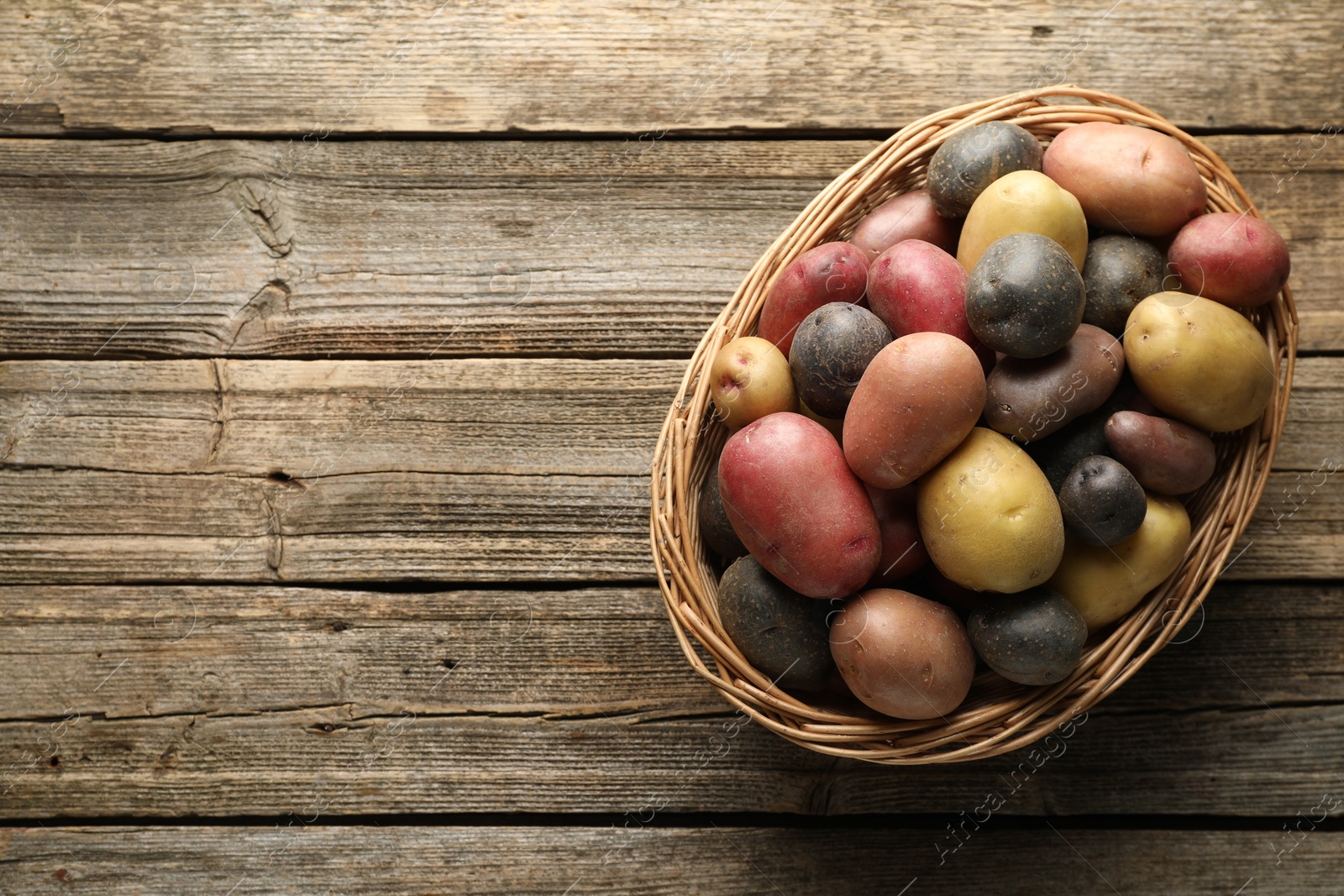Photo of Different types of potatoes in wicker basket on wooden table, top view. Space for text