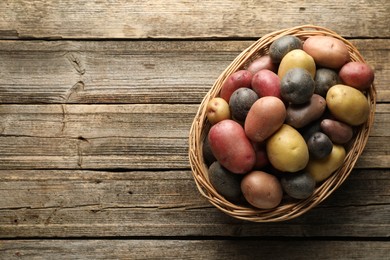 Photo of Different types of potatoes in wicker basket on wooden table, top view. Space for text