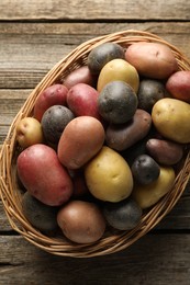 Photo of Different types of potatoes in wicker basket on wooden table, top view