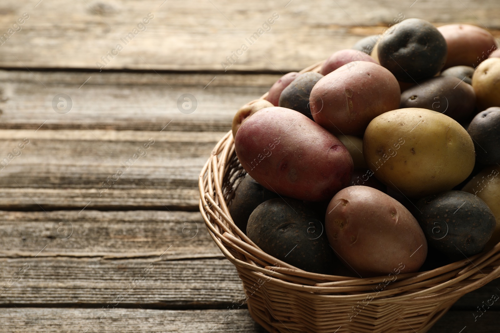 Photo of Different types of potatoes in wicker basket on wooden table, closeup. Space for text