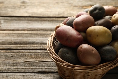 Photo of Different types of potatoes in wicker basket on wooden table, closeup. Space for text