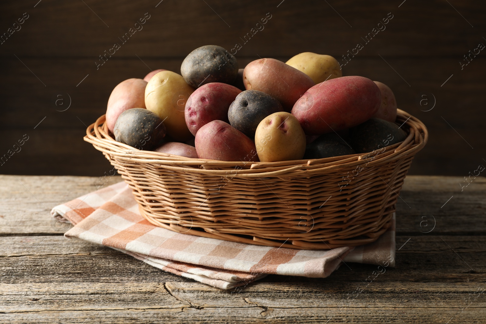 Photo of Different types of potatoes in wicker basket on wooden table