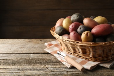 Photo of Different types of potatoes in wicker basket on wooden table, closeup. Space for text
