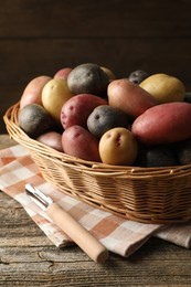 Photo of Different types of potatoes in wicker basket on wooden table, closeup