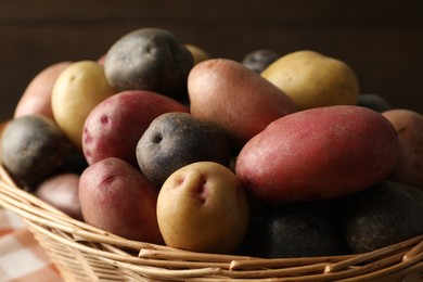 Photo of Different types of potatoes in wicker basket on blurred background, closeup