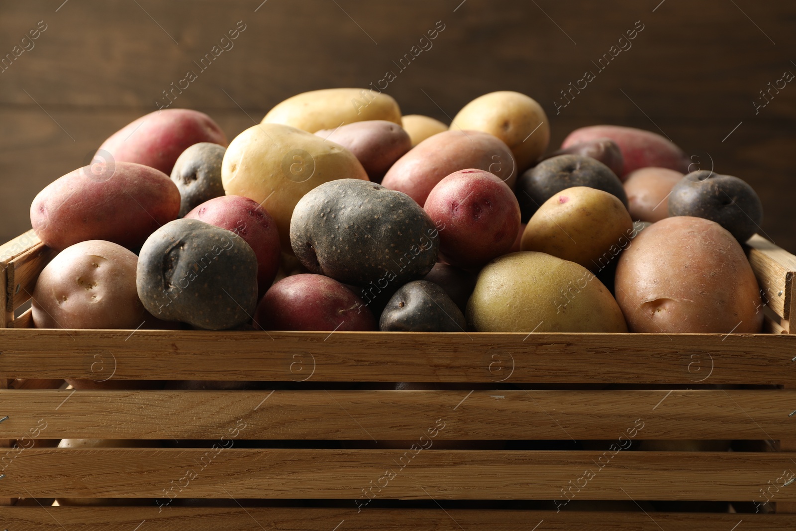 Photo of Different types of potatoes in wooden crate on blurred background, closeup