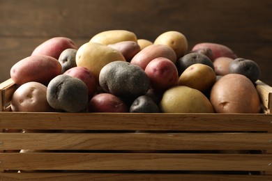 Photo of Different types of potatoes in wooden crate on blurred background, closeup