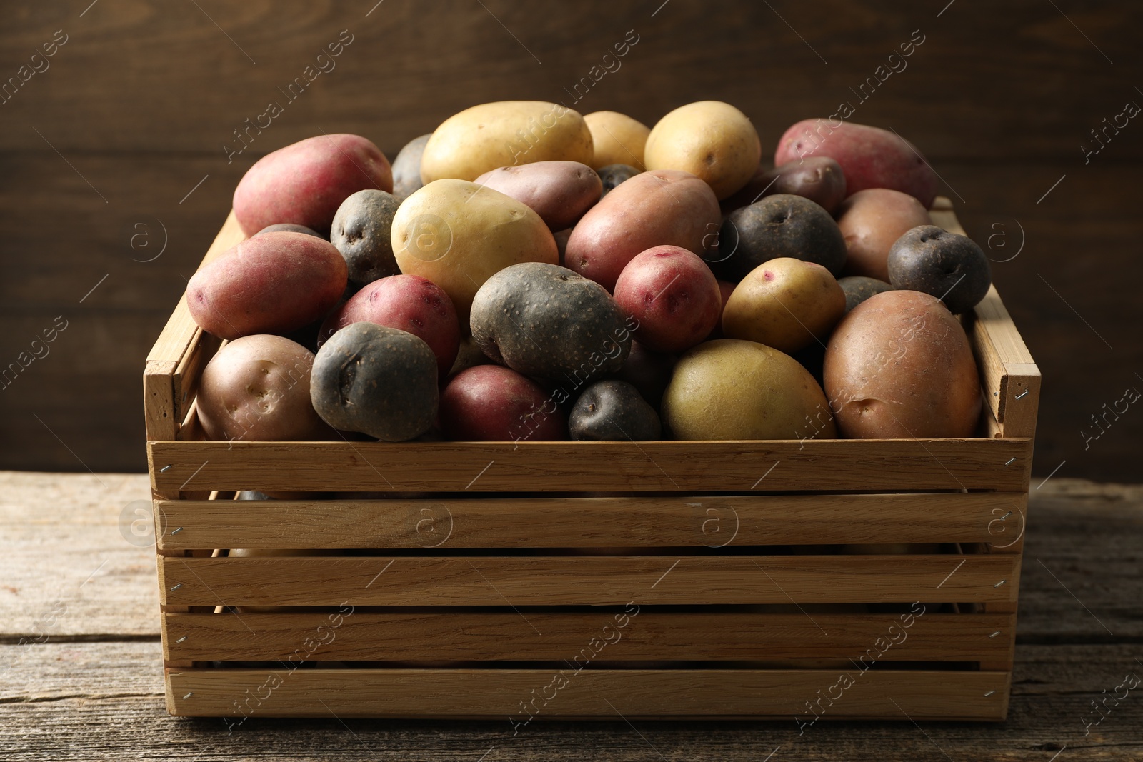Photo of Different types of potatoes in crate on wooden table, closeup
