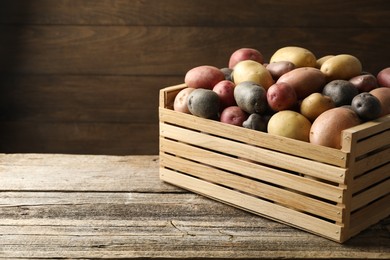 Photo of Different types of potatoes in crate on wooden table, closeup. Space for text