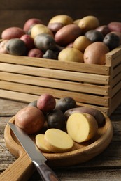 Photo of Different types of potatoes and knife on wooden table, closeup