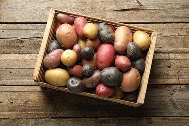 Photo of Different types of potatoes in crate on wooden table, top view