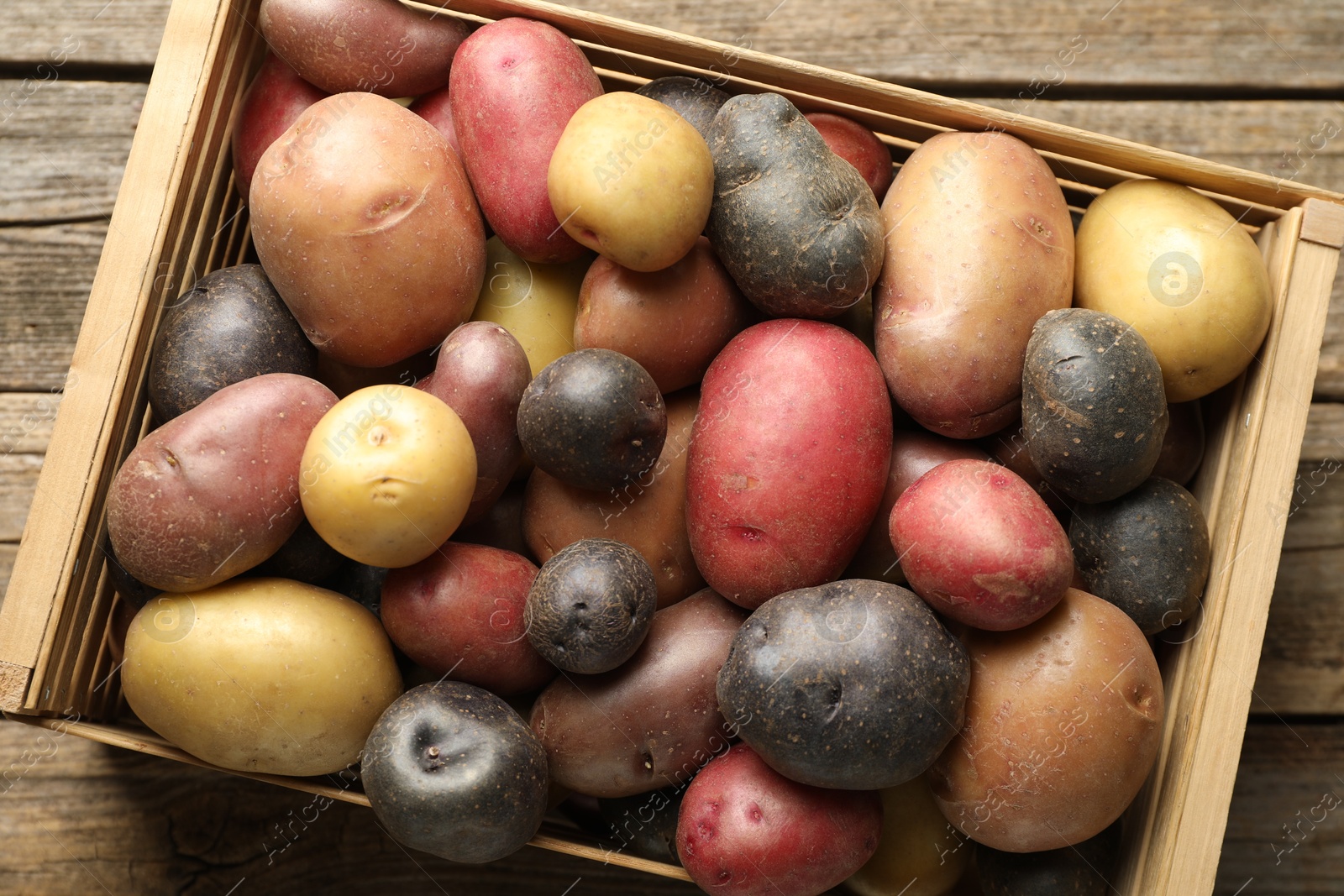 Photo of Different types of potatoes in crate on wooden table, top view
