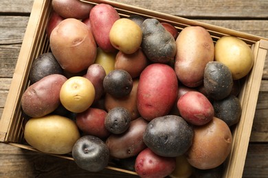 Photo of Different types of potatoes in crate on wooden table, top view