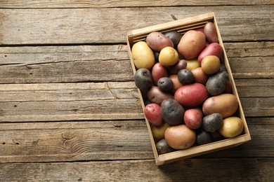 Photo of Different types of potatoes in crate on wooden table, top view. Space for text