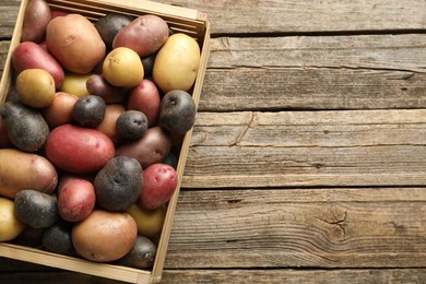 Photo of Different types of potatoes in crate on wooden table, top view. Space for text