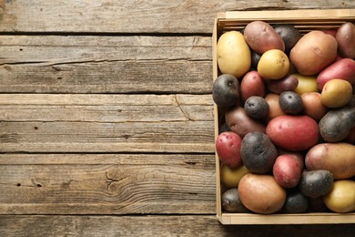 Photo of Different types of potatoes in crate on wooden table, top view. Space for text