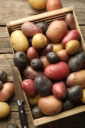 Photo of Different types of potatoes in crate and knife on wooden table, flat lay