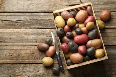 Photo of Different types of potatoes in crate and knife on wooden table, flat lay. Space for text