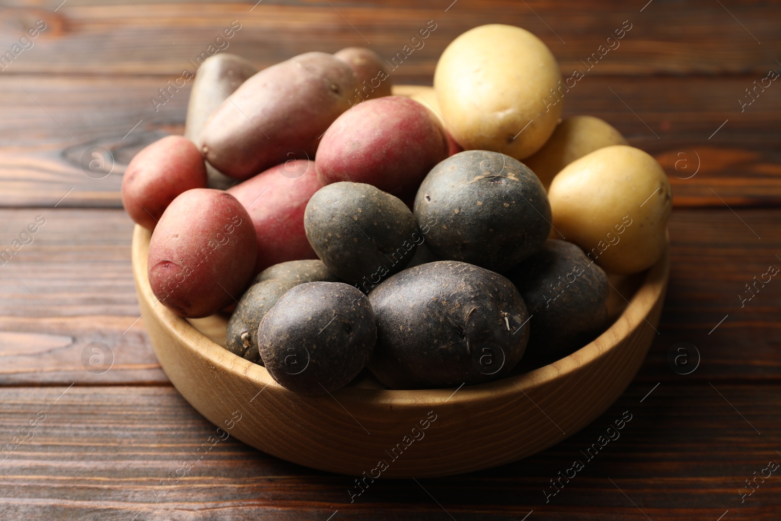 Photo of Different types of potatoes in bowl on wooden table, closeup