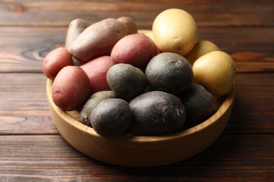 Photo of Different types of potatoes in bowl on wooden table, closeup
