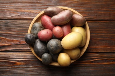 Photo of Different types of potatoes in bowl on wooden table, top view