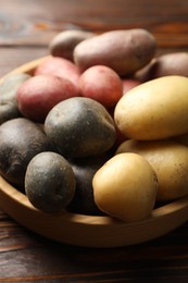 Photo of Different types of potatoes in bowl on wooden table, closeup