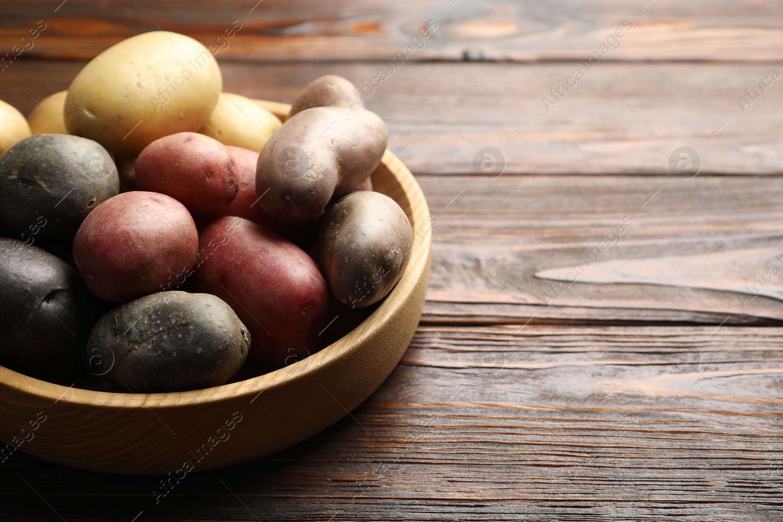 Photo of Different types of potatoes in bowl on wooden table, closeup. Space for text