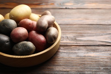 Photo of Different types of potatoes in bowl on wooden table, closeup. Space for text