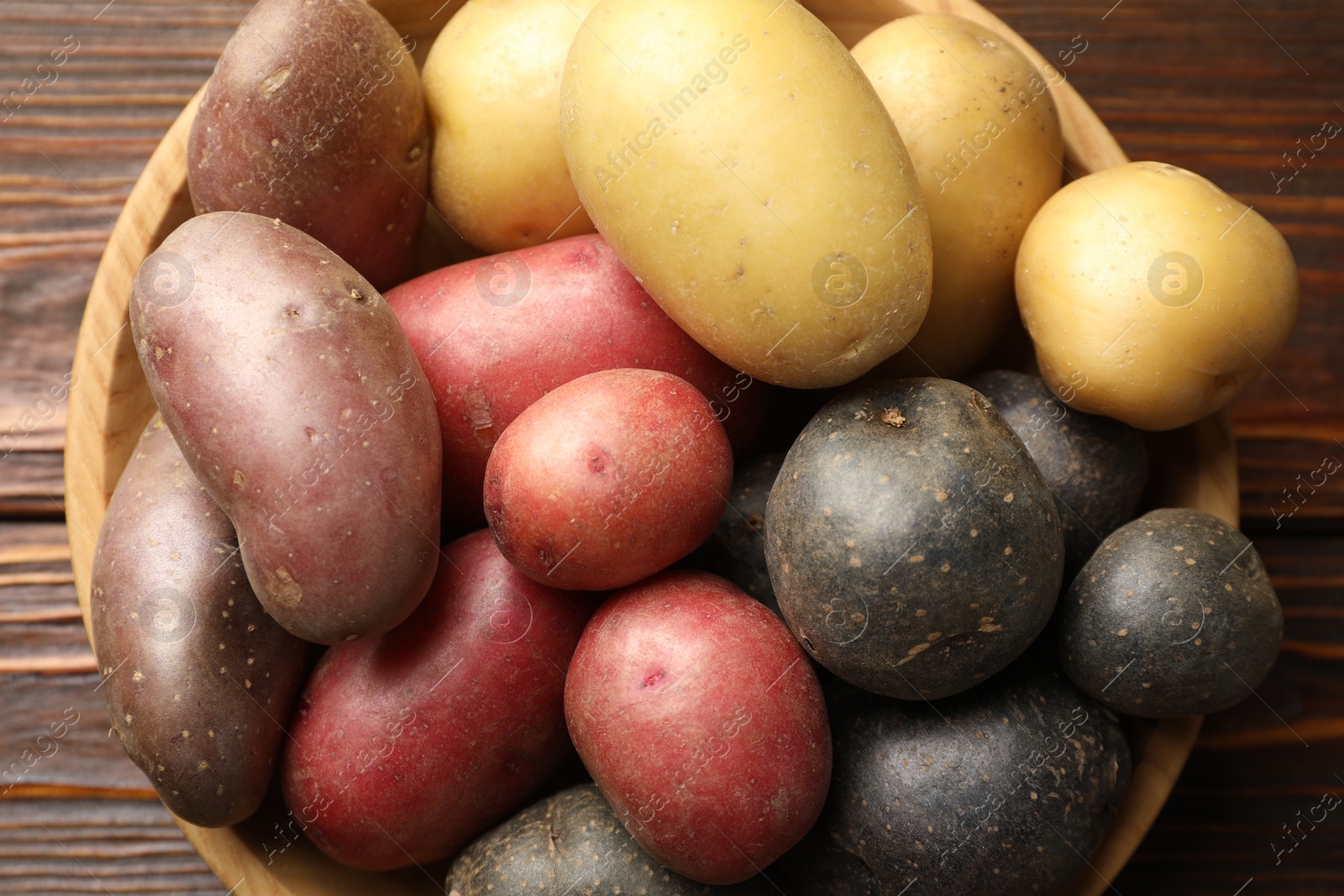 Photo of Different types of potatoes in bowl on wooden table, top view