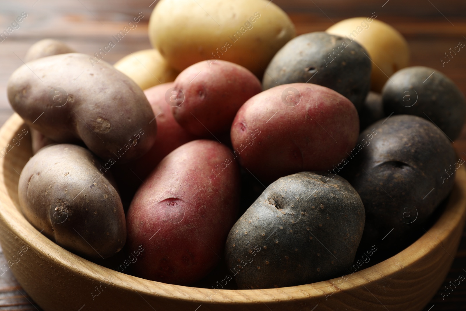 Photo of Different types of potatoes in bowl on table, closeup