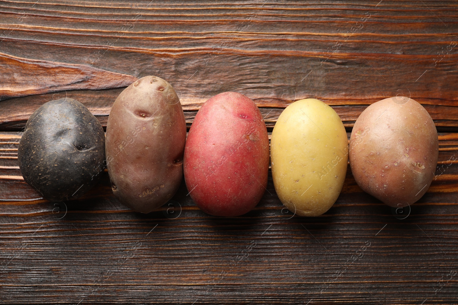 Photo of Different types of potatoes on wooden table, flat lay