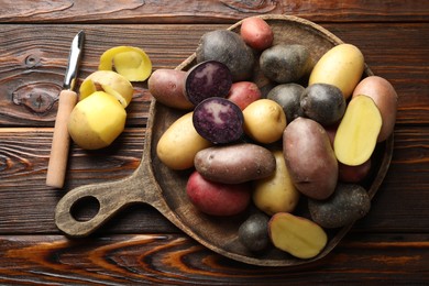 Photo of Different types of potatoes and peeler on wooden table, flat lay